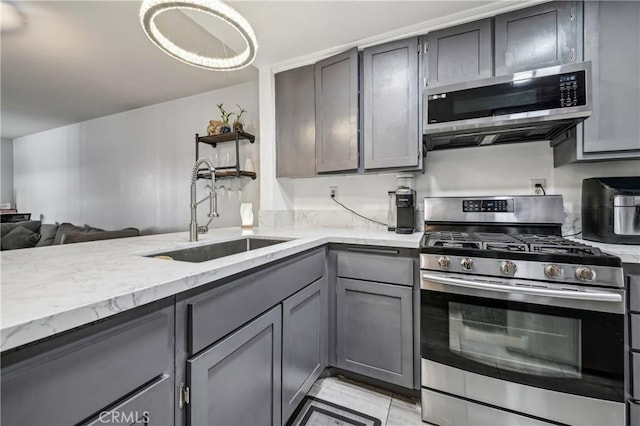 kitchen with gray cabinets, a sink, light stone counters, open floor plan, and appliances with stainless steel finishes