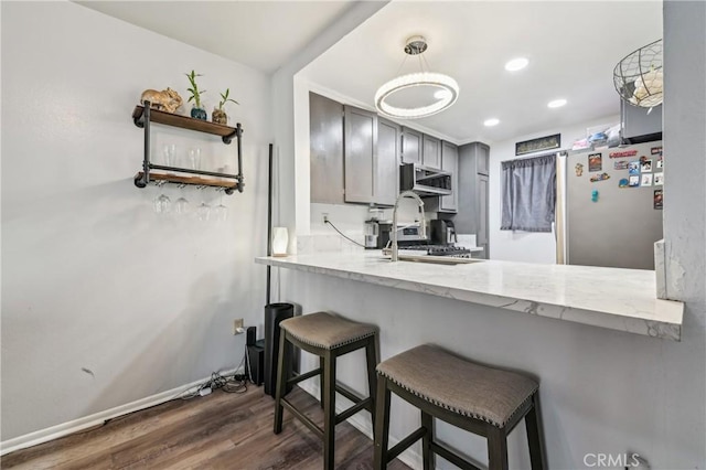 kitchen with a sink, dark wood-style floors, freestanding refrigerator, recessed lighting, and a peninsula