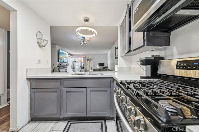 kitchen featuring ventilation hood, light stone countertops, gray cabinets, appliances with stainless steel finishes, and a sink