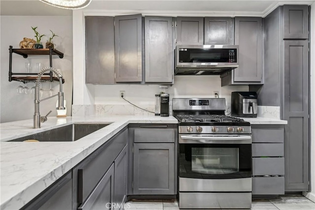 kitchen featuring light stone countertops, gray cabinets, appliances with stainless steel finishes, and a sink