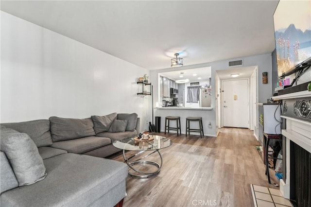 living room with a fireplace with flush hearth, wood finished floors, and visible vents