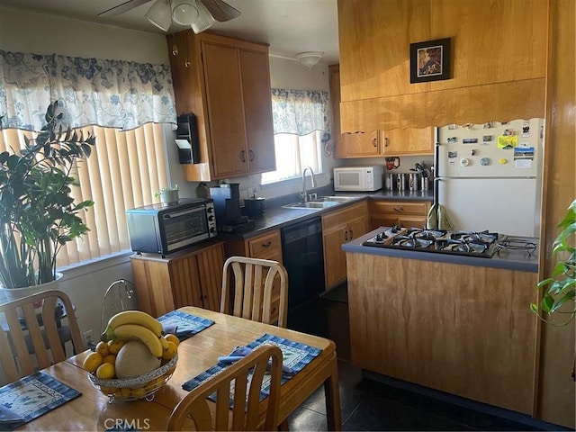 kitchen featuring dark countertops, brown cabinetry, white appliances, a ceiling fan, and a sink