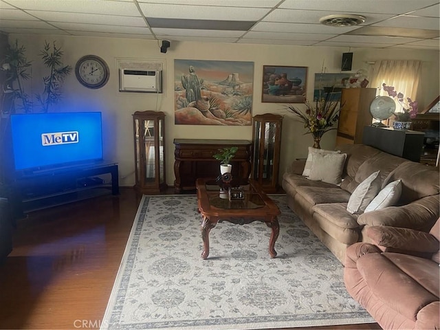 living room featuring a paneled ceiling, visible vents, a wall unit AC, and wood finished floors