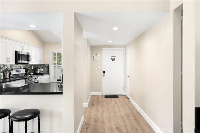 kitchen featuring a breakfast bar, stainless steel appliances, white cabinetry, dark countertops, and backsplash