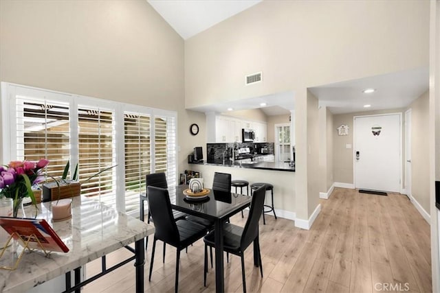 dining area featuring visible vents, baseboards, recessed lighting, light wood-style flooring, and a towering ceiling