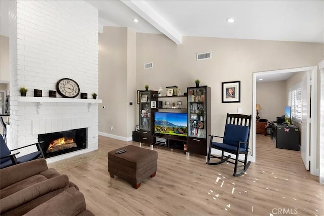 living area featuring visible vents, beamed ceiling, a fireplace, and wood finished floors