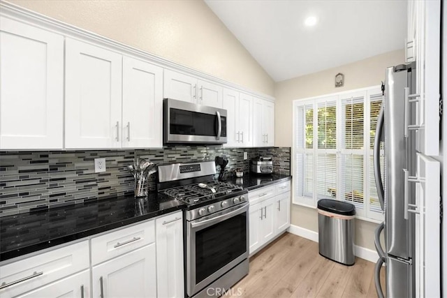 kitchen with vaulted ceiling, white cabinets, appliances with stainless steel finishes, light wood-type flooring, and backsplash