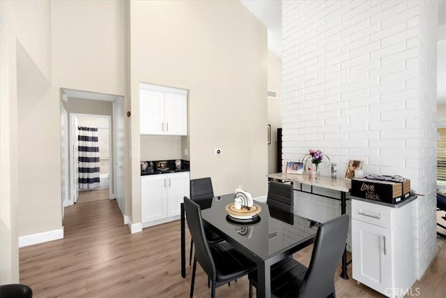 dining room with visible vents, light wood-style flooring, a high ceiling, and baseboards