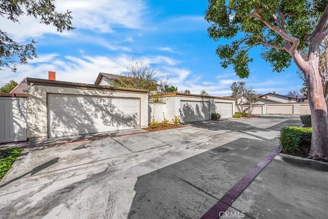 exterior space with fence, stucco siding, a chimney, a garage, and driveway