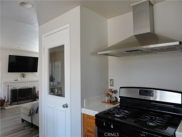 10402 Via Pajaro, Moreno Valley, CA 92557 - kitchen with gas stove, tile countertops, wall chimney range hood, a brick fireplace, and wood finished floors