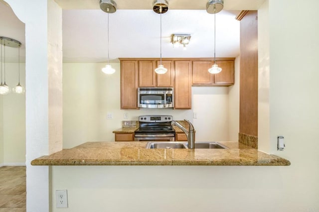 kitchen featuring light stone counters, a peninsula, stainless steel appliances, and a sink