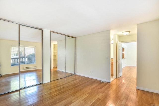 unfurnished bedroom featuring light wood-style floors, baseboards, two closets, and baseboard heating