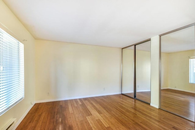 unfurnished bedroom featuring multiple windows, wood finished floors, multiple closets, and a baseboard radiator