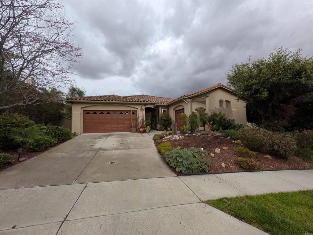 mediterranean / spanish-style house featuring a tiled roof, an attached garage, driveway, and stucco siding