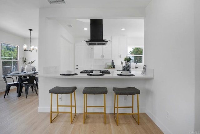 kitchen with a breakfast bar, a peninsula, light wood-style floors, white cabinetry, and island range hood