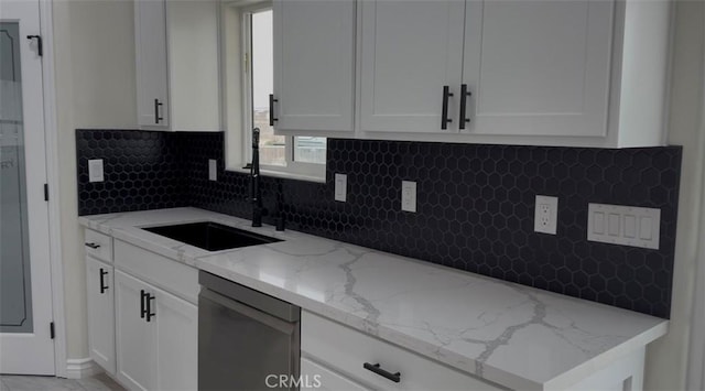 kitchen with backsplash, light stone countertops, stainless steel dishwasher, white cabinetry, and a sink