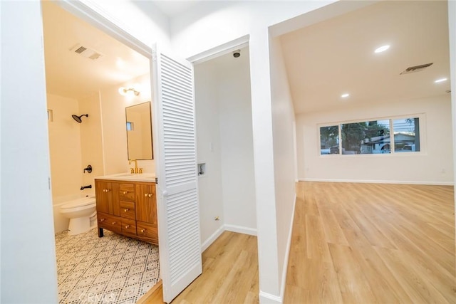 hallway featuring baseboards, visible vents, and light wood finished floors