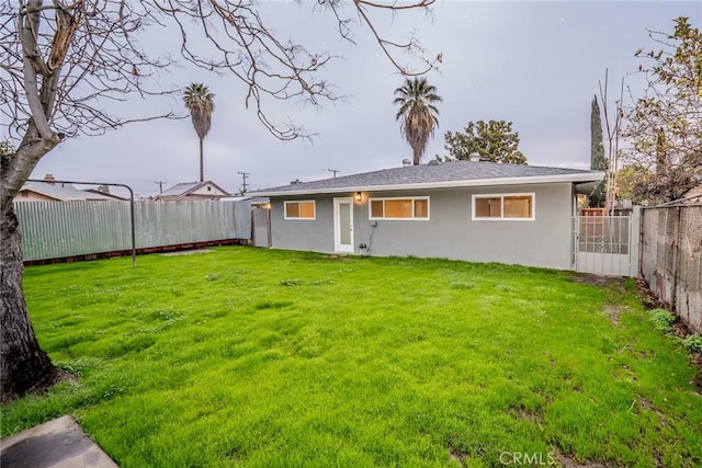 rear view of house with a lawn, a fenced backyard, and stucco siding