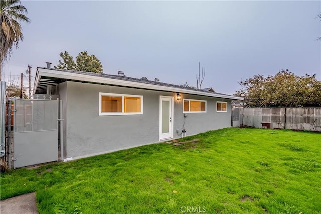 back of house featuring stucco siding, a yard, and fence