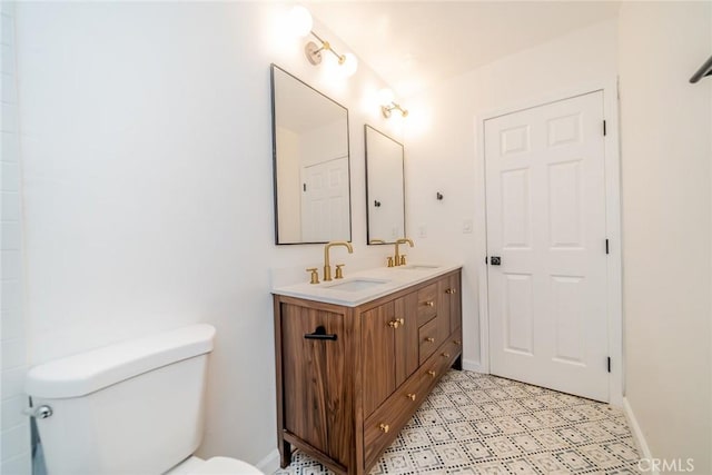 bathroom featuring double vanity, toilet, baseboards, and a sink