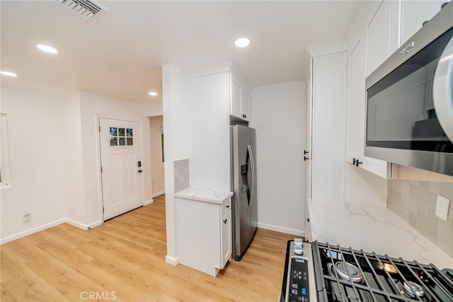 kitchen with light stone countertops, visible vents, light wood-style flooring, appliances with stainless steel finishes, and white cabinetry