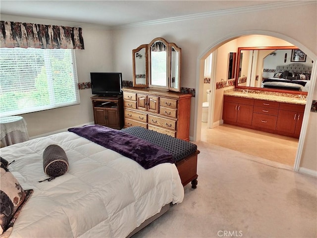 bedroom featuring ensuite bath, light colored carpet, arched walkways, and ornamental molding