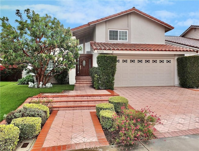 view of front of house featuring a front lawn, a tiled roof, stucco siding, decorative driveway, and a garage