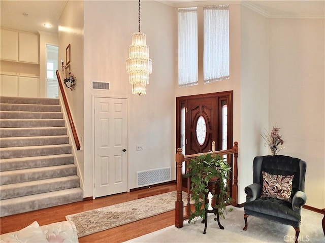 entryway featuring a chandelier, visible vents, crown molding, and stairs