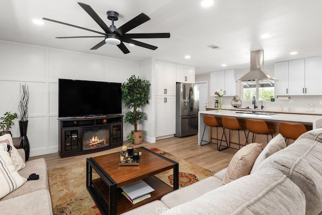 living room featuring visible vents, light wood finished floors, a ceiling fan, recessed lighting, and a decorative wall