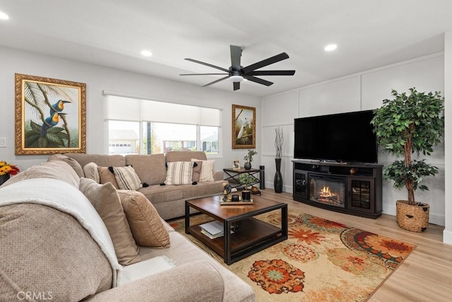 living area featuring a glass covered fireplace, recessed lighting, light wood-type flooring, and a ceiling fan