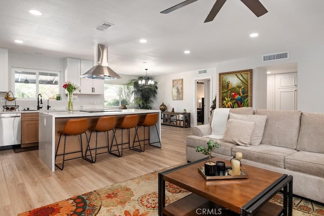 living room featuring ceiling fan with notable chandelier, visible vents, and light wood-type flooring