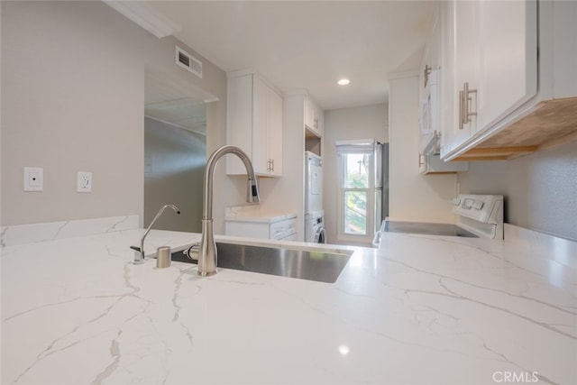 kitchen featuring stacked washer and dryer, a sink, white cabinets, range, and light stone countertops