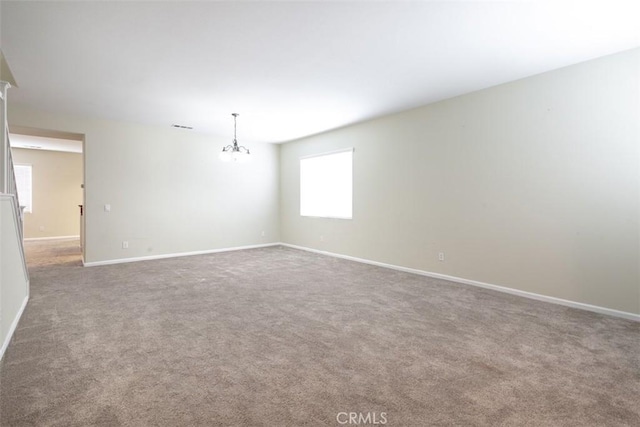 carpeted spare room with visible vents, baseboards, and a notable chandelier