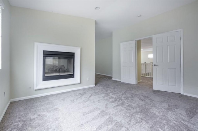 unfurnished living room featuring baseboards, a glass covered fireplace, and carpet flooring