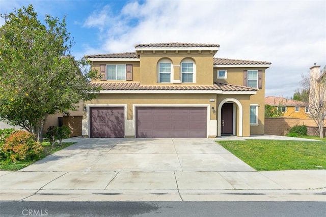 mediterranean / spanish-style home featuring stucco siding, driveway, a front yard, a garage, and a tiled roof