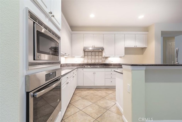 kitchen with dark countertops, white cabinets, under cabinet range hood, and stainless steel appliances