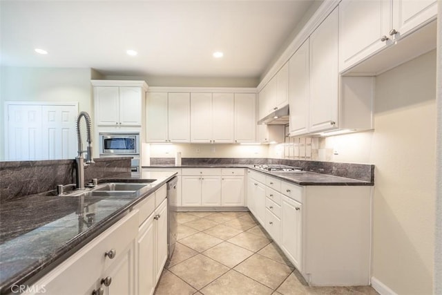 kitchen with under cabinet range hood, a sink, white cabinetry, dark stone counters, and appliances with stainless steel finishes