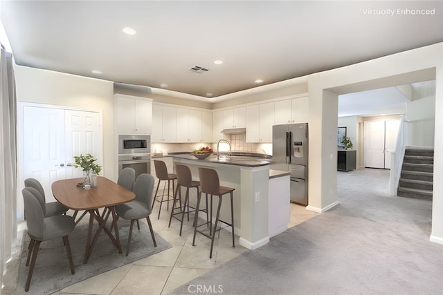 kitchen with dark countertops, tasteful backsplash, a center island with sink, light tile patterned floors, and stainless steel appliances