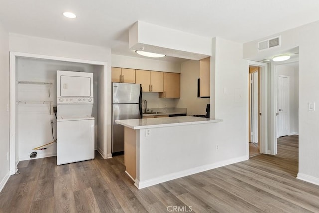 kitchen with light brown cabinets, light countertops, stacked washer and clothes dryer, freestanding refrigerator, and wood finished floors