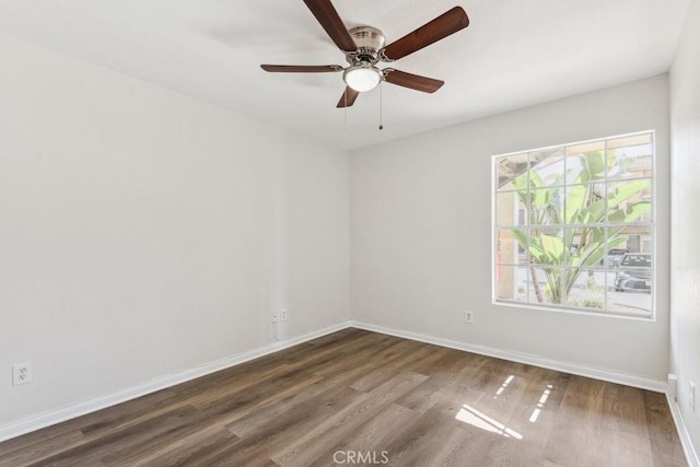 spare room with dark wood-style floors, a ceiling fan, and baseboards