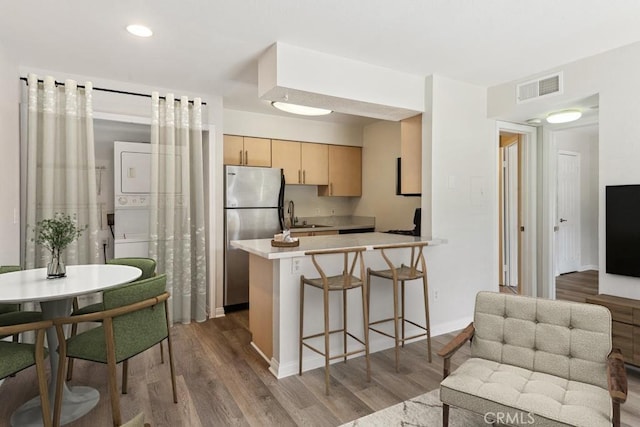 kitchen featuring visible vents, light brown cabinetry, wood finished floors, freestanding refrigerator, and a peninsula
