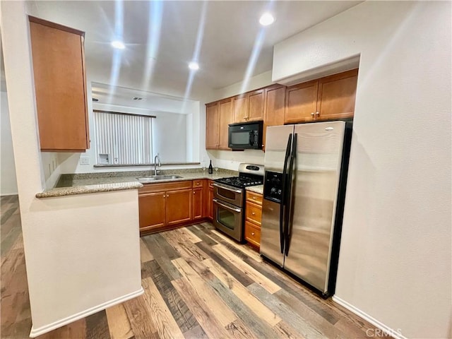 kitchen with wood finished floors, recessed lighting, a sink, stainless steel appliances, and brown cabinets