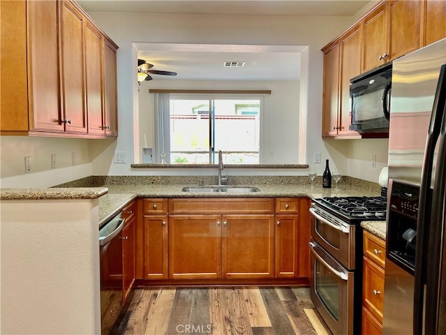 kitchen featuring light stone counters, a ceiling fan, wood finished floors, a sink, and appliances with stainless steel finishes