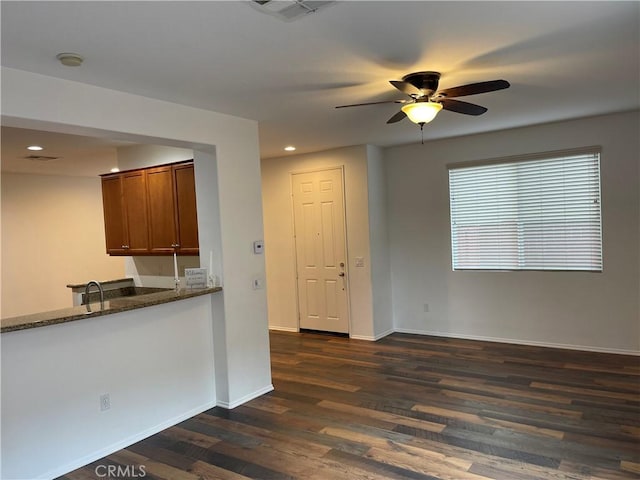 kitchen with dark wood-style floors, brown cabinetry, baseboards, dark stone counters, and ceiling fan