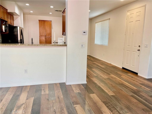 kitchen with light stone counters, visible vents, black microwave, refrigerator with ice dispenser, and brown cabinets