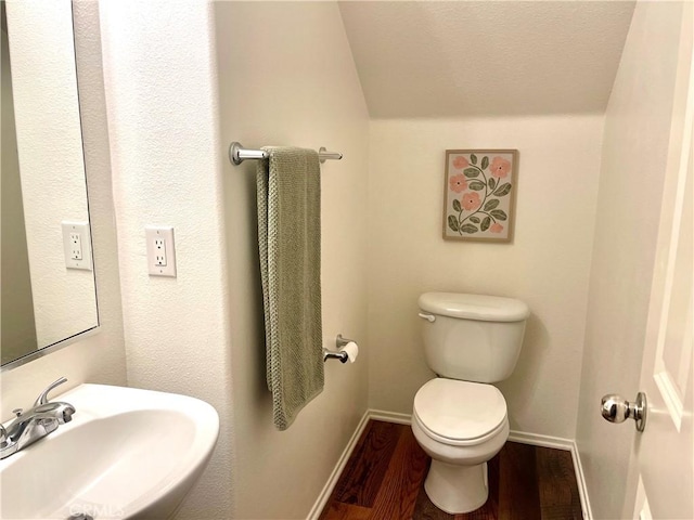 half bathroom with a sink, baseboards, toilet, and wood finished floors