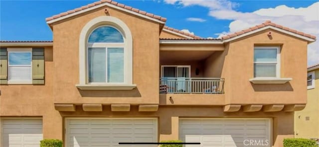 view of front of house featuring stucco siding, an attached garage, a tile roof, and a balcony