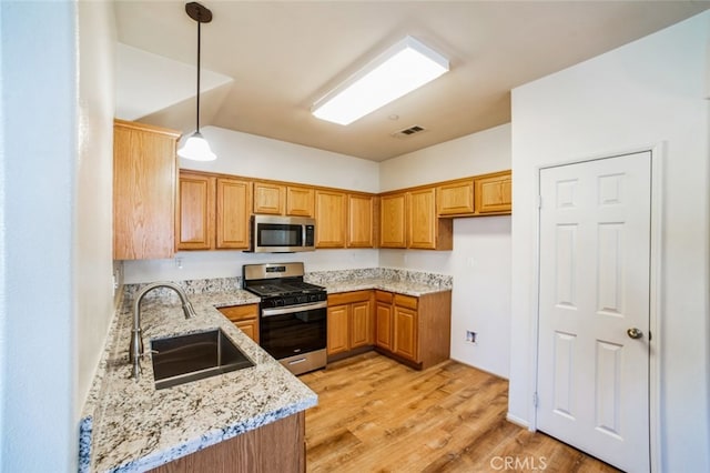 kitchen with visible vents, a sink, stainless steel appliances, light stone countertops, and hanging light fixtures