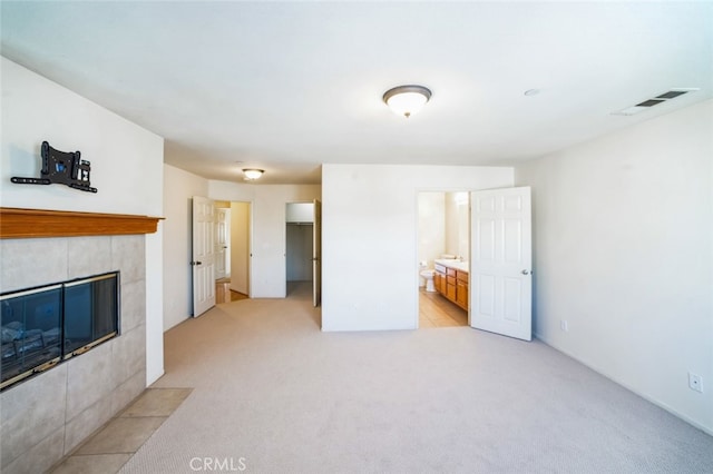 unfurnished living room with a tiled fireplace, visible vents, and light carpet