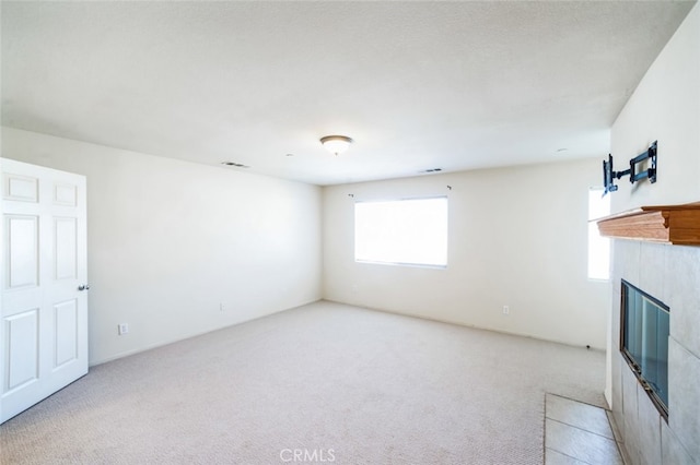 unfurnished living room featuring a tiled fireplace, light colored carpet, and visible vents